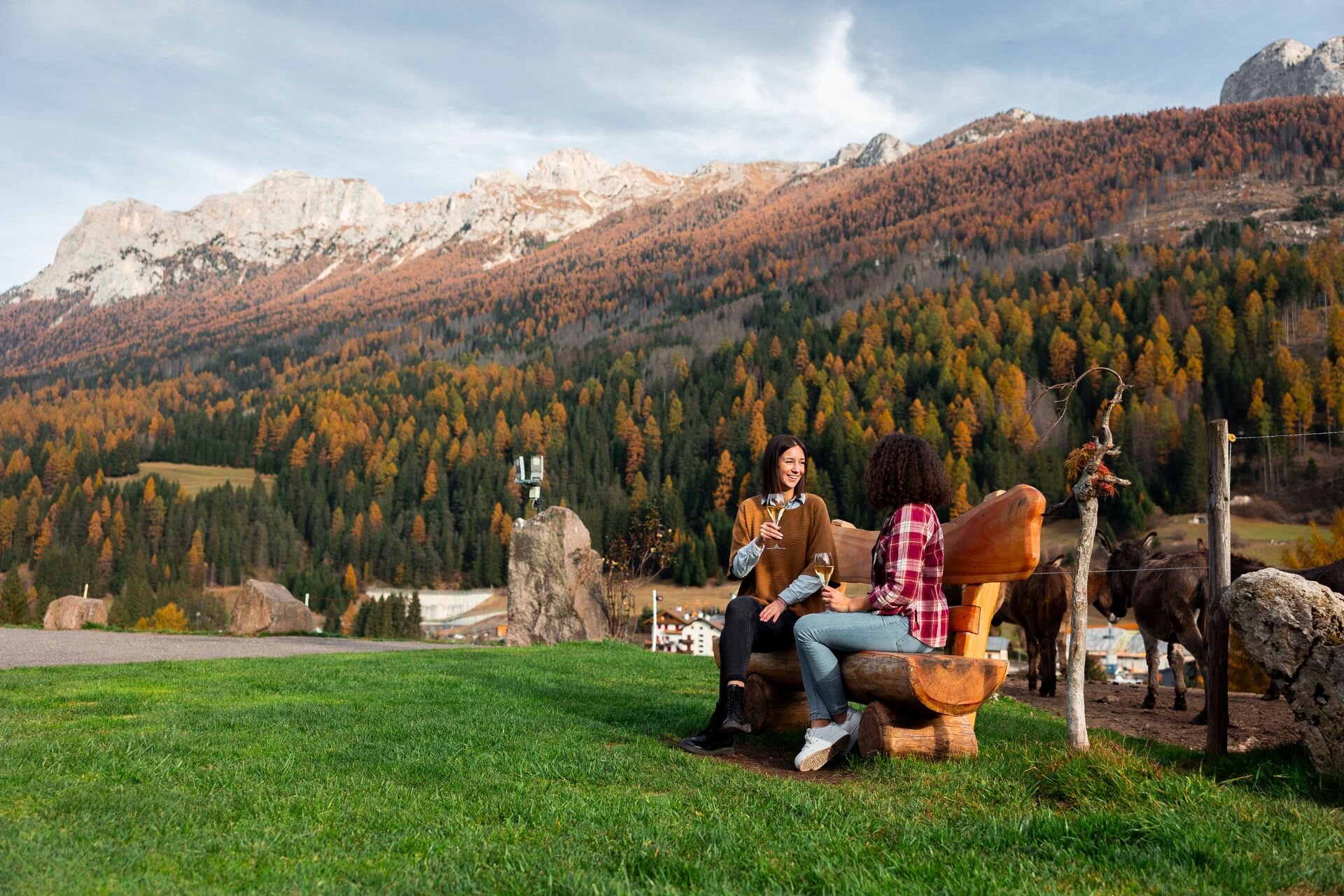 Mangiare e bere in una malga in Val di Fassa | © Archivio Immagini ApT Val di Fassa - Federico Modica Coppia seduta su una panchina di una malga beve con le dolomiti autunnali sullo sfondo | © Archivio Immagini ApT Val di Fassa - Federico Modica