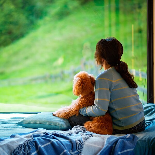 Alloggi | © Archivio Immagini ApT Val di Fassa Persona che guarda fuori dalla finestra con il suo cane | © Archivio Immagini ApT Val di Fassa